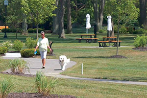 retiree walks dog on walking path at Athens Crossing